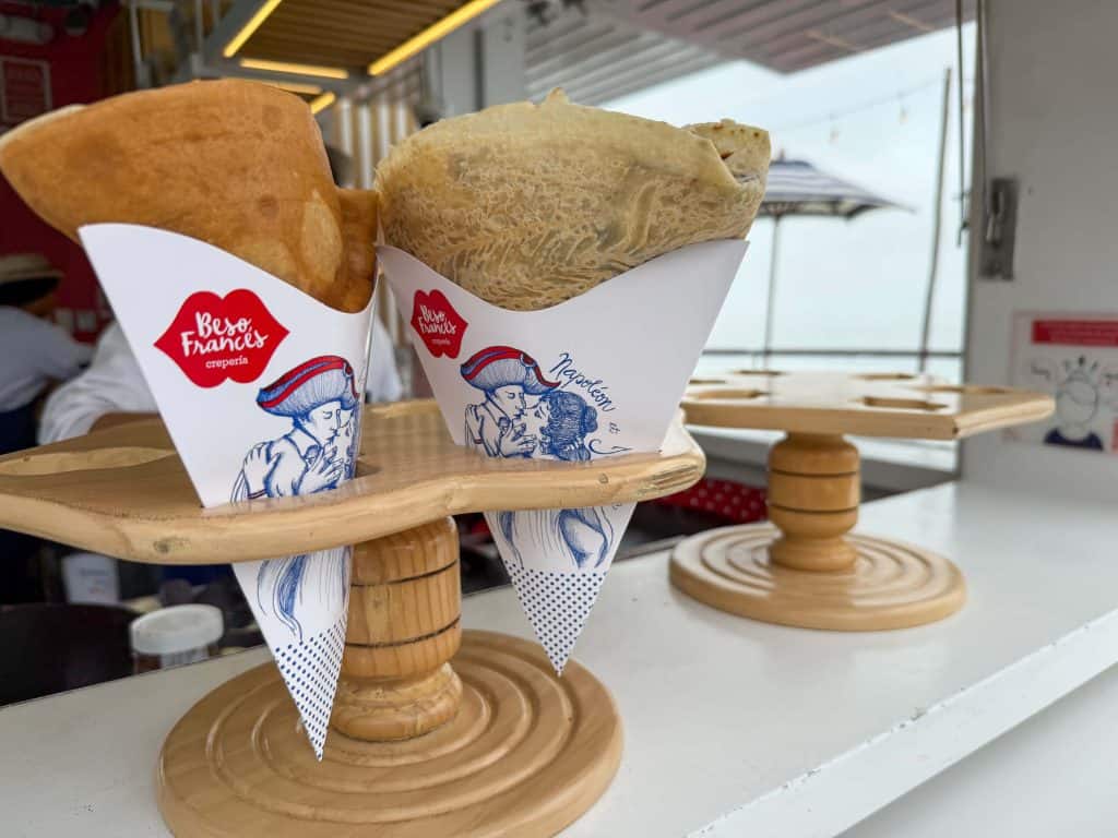 Two delicious crepes in cute white handheld paper pockets with the Besos Frances logo of a couple kissing.