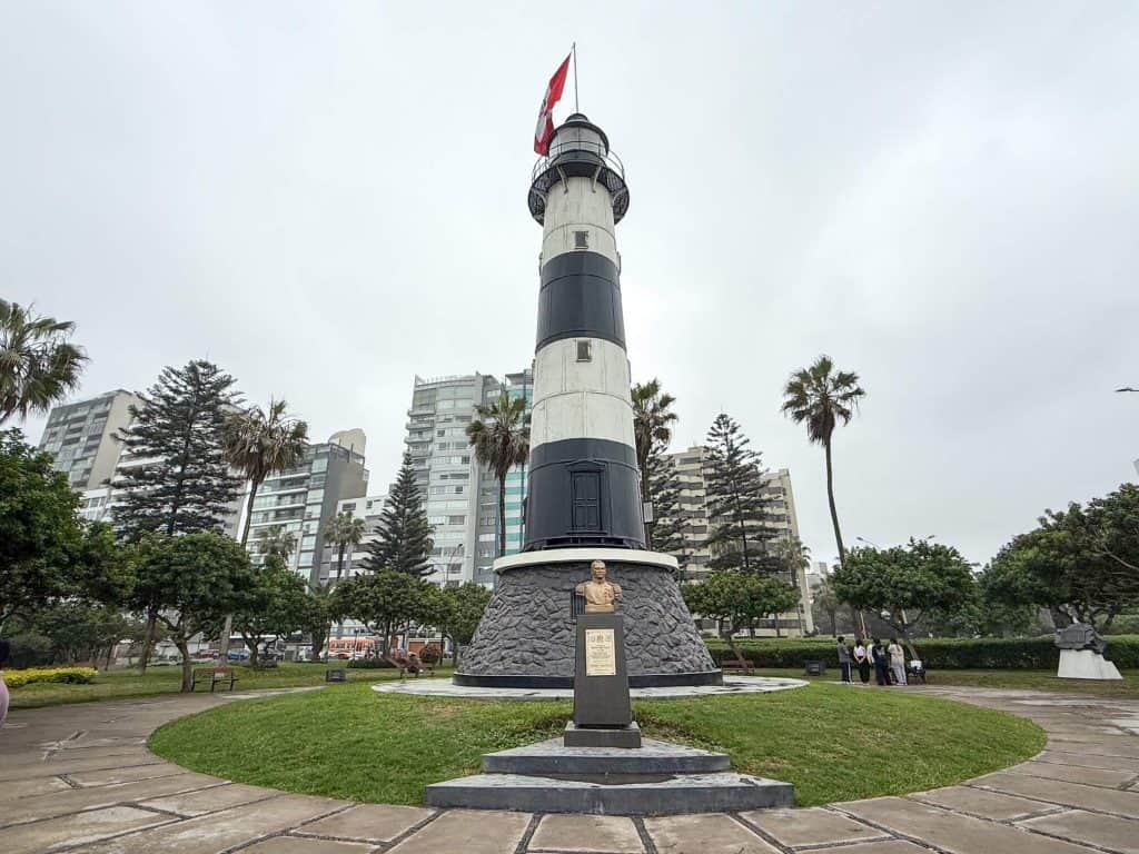 Standing at the base of a black and white striped lighthouse along the cliffs of Malecon Miraflores walkway in Lima.