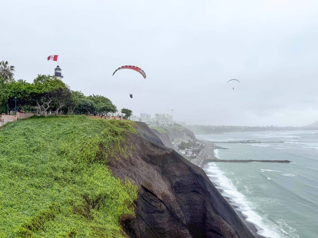 View of two hanggliders soaring over the cliffs, Pacific Ocean and lighthouse on a cloudy day in Lima, Peru.