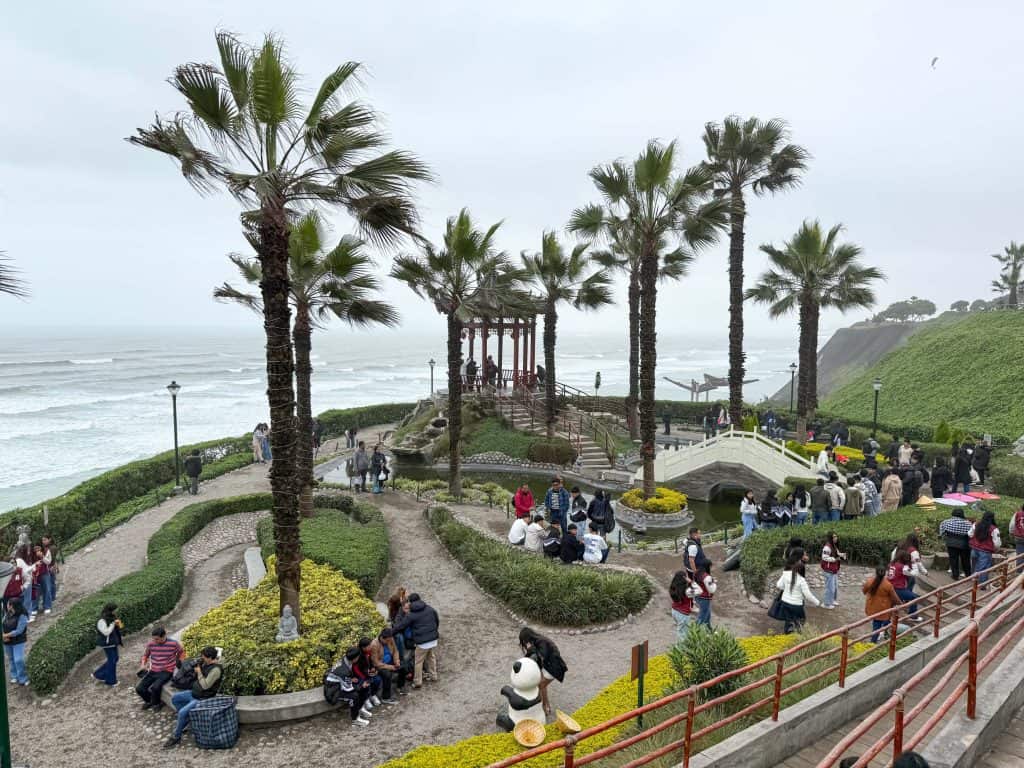 Looking down at Chinese Park along the Pacific Ocean in Lima's Malecon Miraflores with its palm tree, manicured garden, a panda bear statue, coy pond, gazebo, and small bridge.