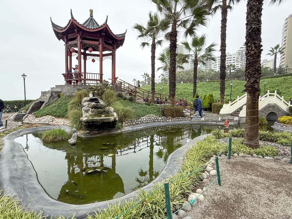 A beautifully manicured Chinese garden with a small coy pond, gazebo, white bridge and palm trees at Chinese Park along the Pacific Ocean in Lima, Peru.