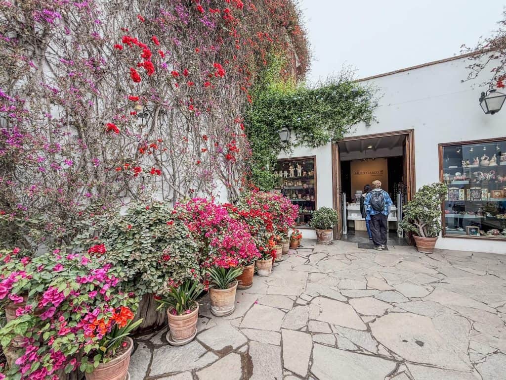 The entry courtyard at Larco Museum with a wall covered in flower vines and pots of flowers lining the entrance in Lima.