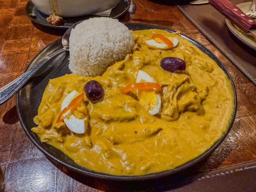 A plate of Aji de Gallina Peruvian dish with rice which has a yellow color with chicken, hard boiled eggs, olives, and seasonings.
