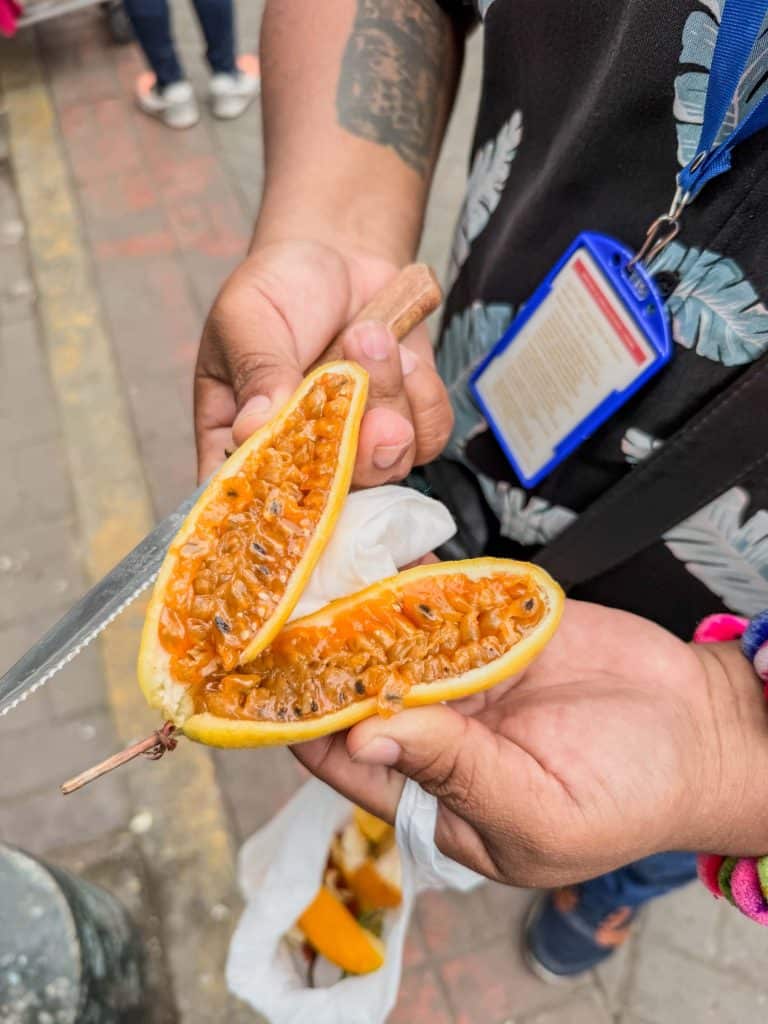 An elongated orange colored fruit similar to a passion fruit cut open to show the flesh and seeds at Surquillo market in Lima.