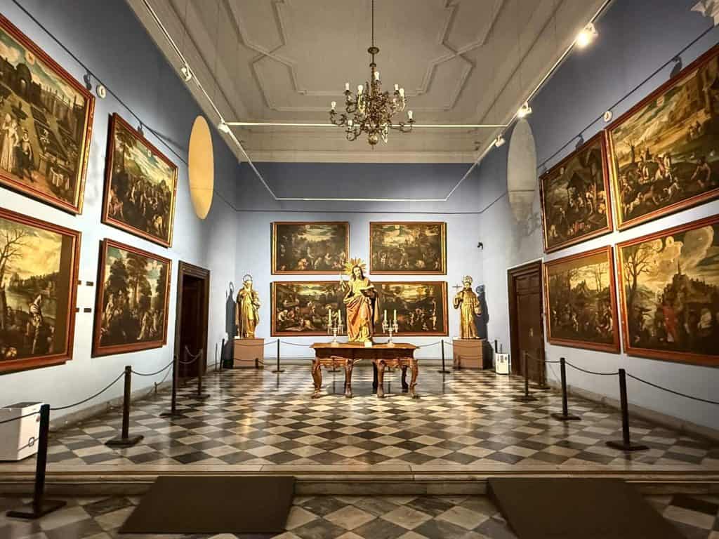 Inside room at the Lima Cathedral part of the museum with several paintings against blue walls and black and white checkered flooring.