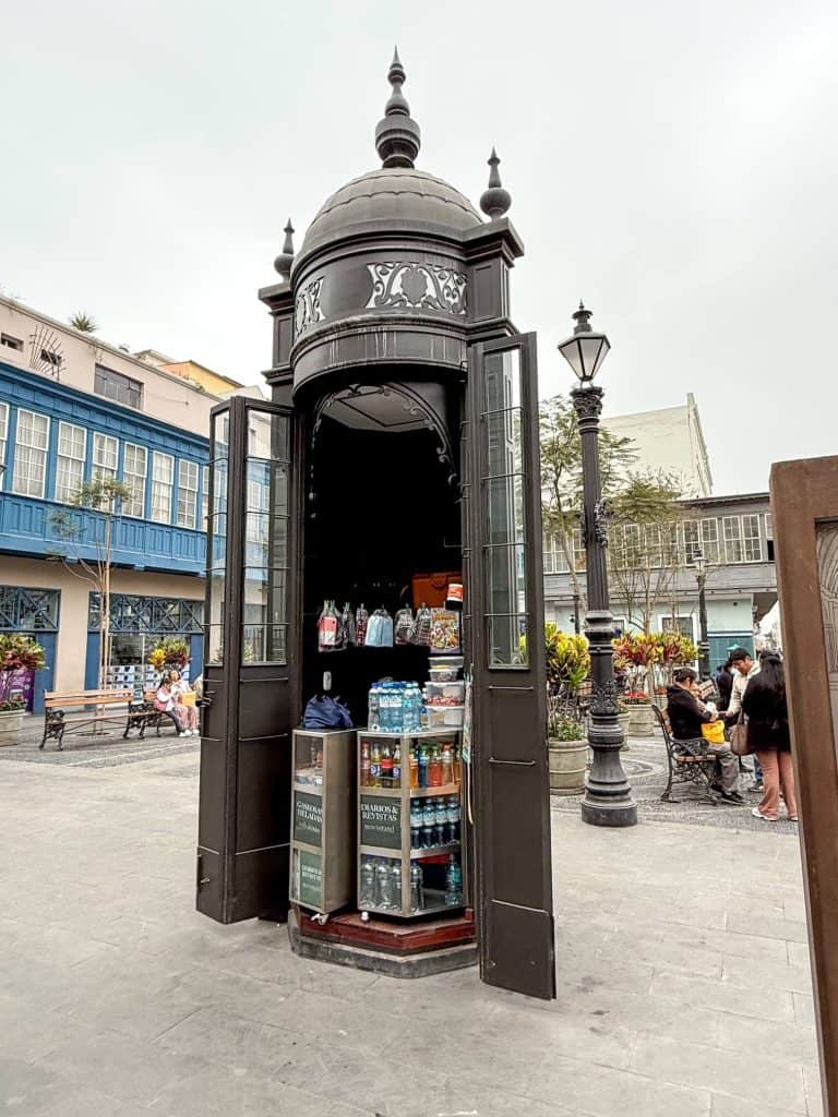 A tiny news stand with snacks and drinks in a tall and thin historic iron enclosure in the middle of a small square near Plaza Major in Lima.