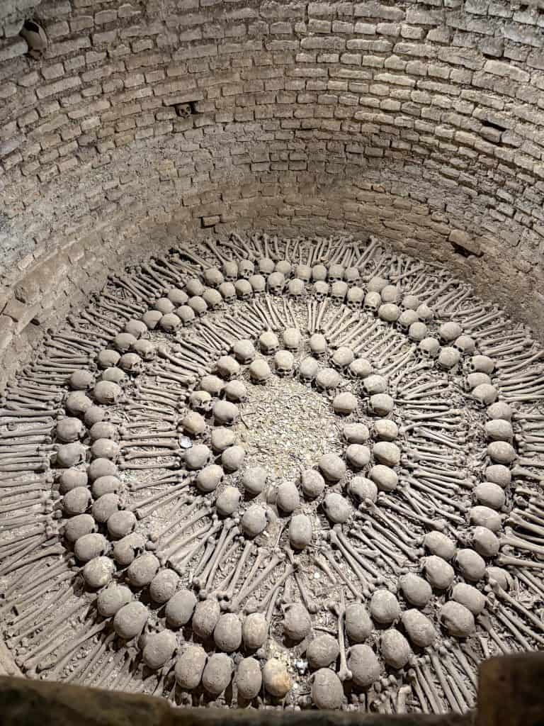 Looking down into a round hole with hundreds of bones and skulls arranged in a pattern in the catacombs underneath the convent and church of San Francisco in Lima, Peru.