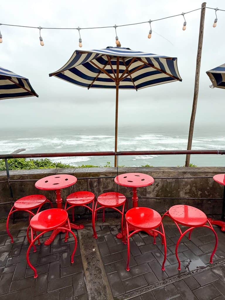 Bright red stools and table with blue and white umbrellas along the cliff overlooking the Pacific Ocean at Besos Frances in the Miraflores neighborhood of Lima.