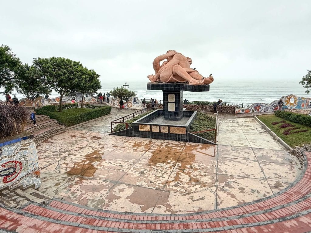 The kissing statue of two people in middle of a curved step seating area with views of the Pacific Ocean beyond at Parque Amor in Lima, Peru.