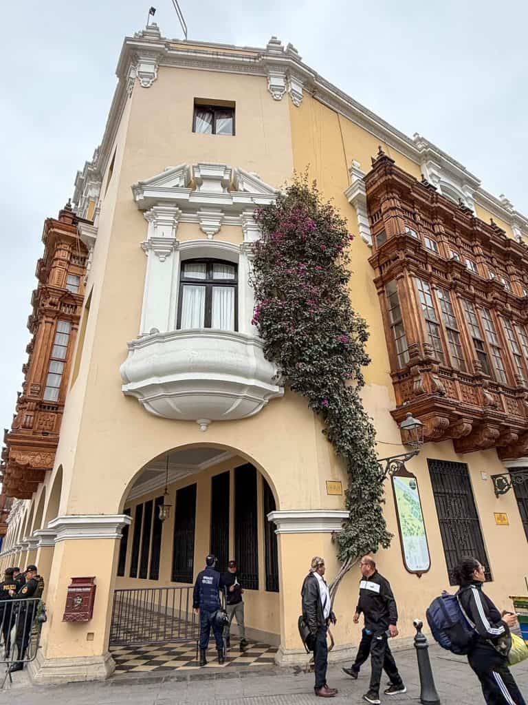 A beautiful historic building along Plaza Mayor in Lima's historic district painted in a pale yellow and with enclosed wooden balconies and pretty flower vines along the side in Lima, Peru.