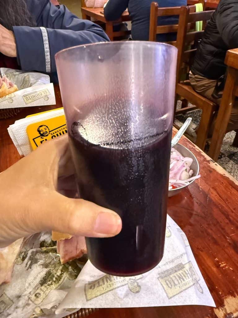 Holding a glass of chicha morada, a dark purple drink made from fermented purple corn.