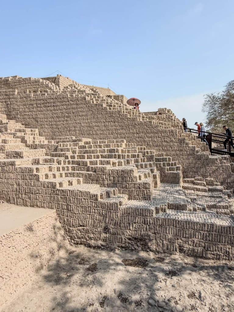 A side view of the Huaca Pucllana pyramid with the layers of stacked adobe blocks as people walk up in Lima, Peru neighborhood of Miraflores.